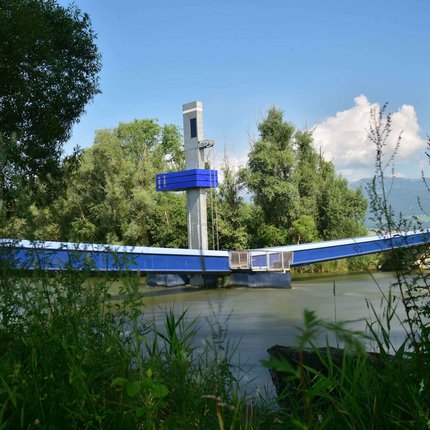 Blue drawbridge over a river, surrounded by trees and vegetation