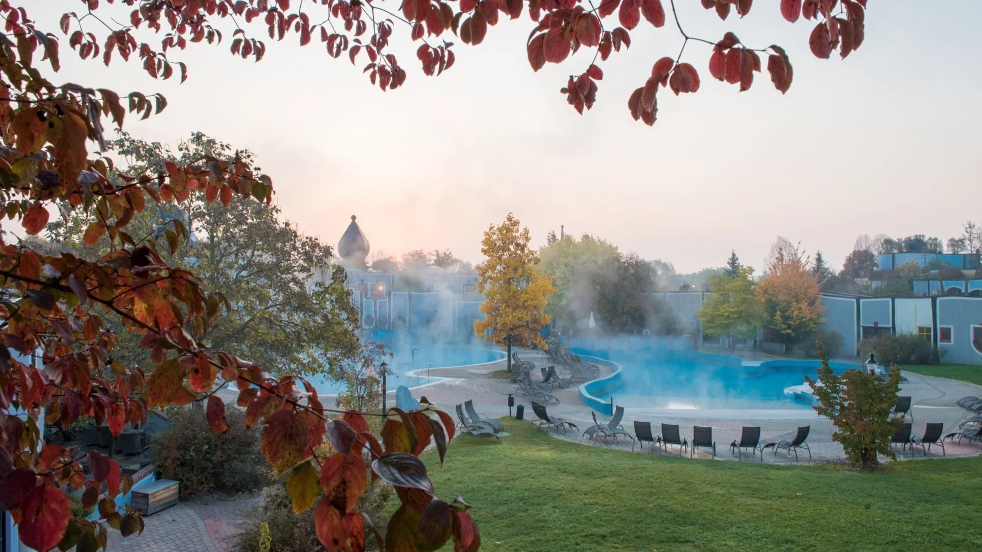 Thermaalbad met stoom uit het zwembad en rode herfstbladeren op de voorgrond