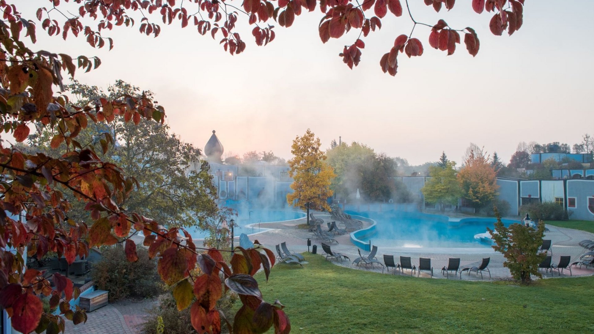 Thermal spa with steaming pool and autumn red leaves in the foreground