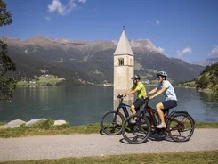 Twee fietsers bij verzonken kerktoren in bergmeer op zonnige dag