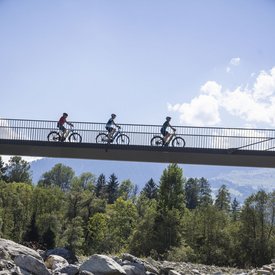 Three cyclists riding on a bridge over a rocky river