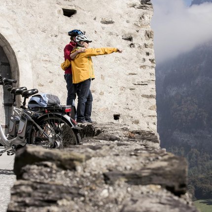 Two cyclists in helmets looking over castle wall at foggy valley