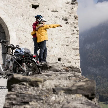 Twee fietsers met helmen kijken vanaf kasteelmuur naar mistige vallei