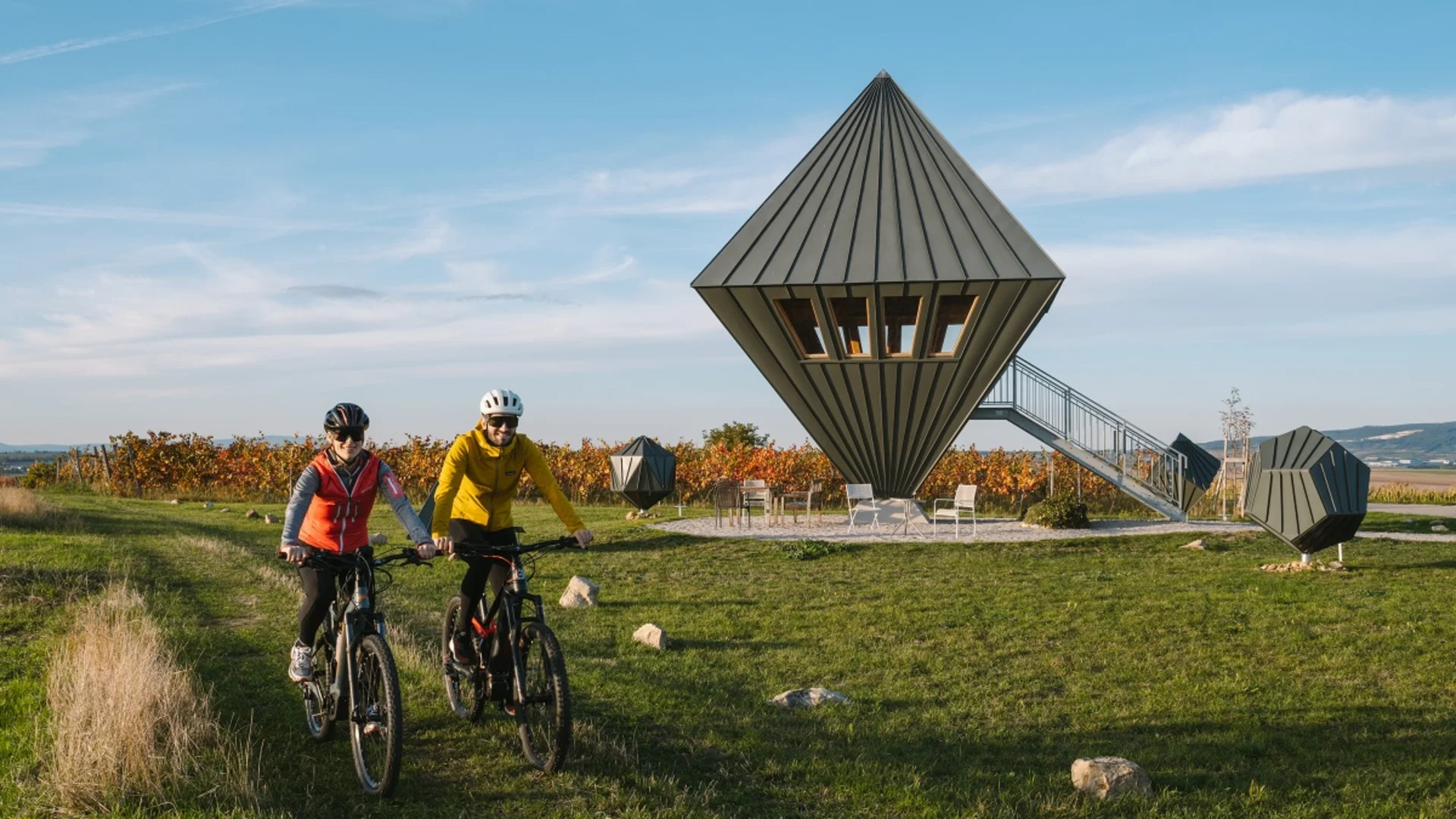 Twee fietsers op een pad bij moderne puntige boomhutten buiten