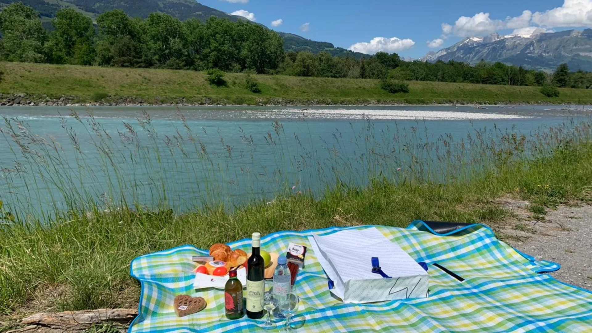 Picknickdecke mit Essen und Getränken neben Fluss und Bergen