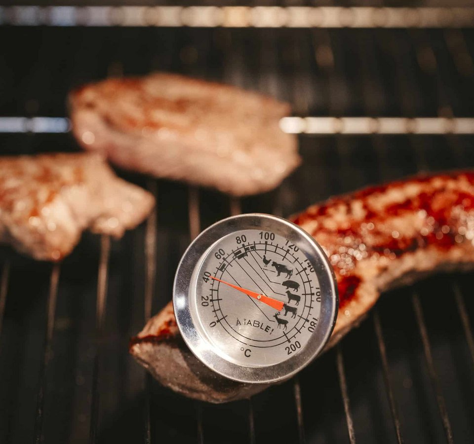 Meat on grill with thermometer measuring temperature