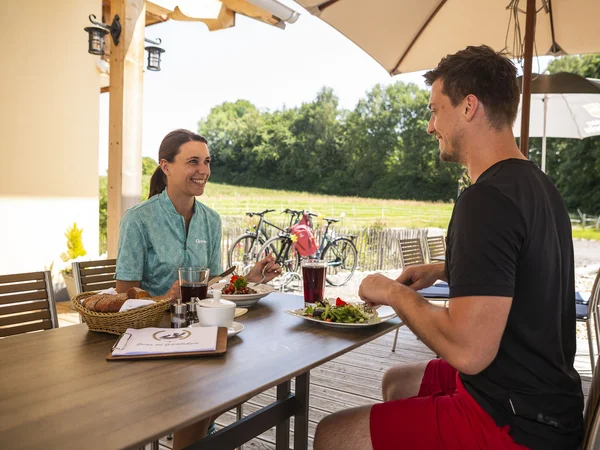 Kulinarisch Radeln rund um den Chiemsee © Velontour Zwei Personen essen draußen an einem Tisch mit Fahrrädern im Hintergrund