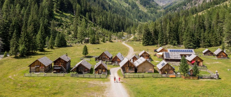 Small wooden cabins in a green valley surrounded by mountains and pine forests