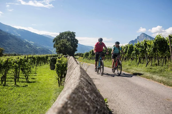 Heidiland: Von Wein bis Thermalwasser © Velontour Zwei Radfahrer auf Landstraße durch Weinberge mit Bergen im Hintergrund