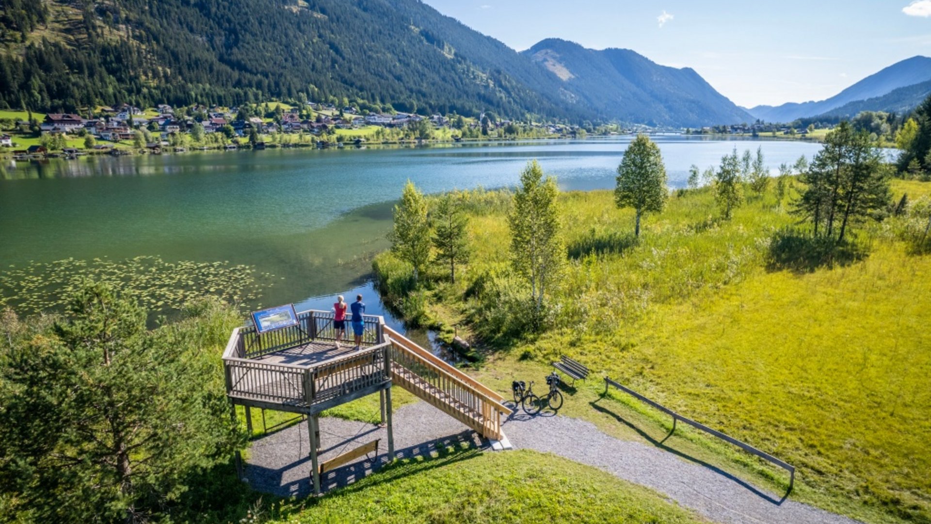 Viewing platform by lake with mountains and bicycles in lush green valley