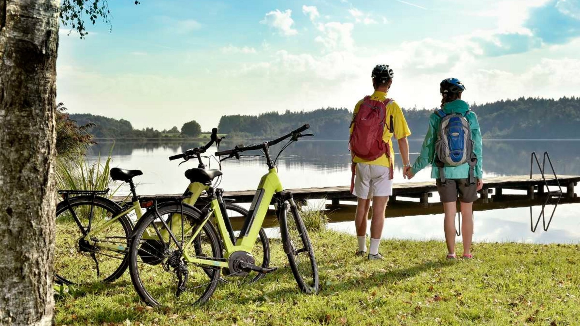 Couple holding hands at lakeside with bikes parked nearby on a sunny day