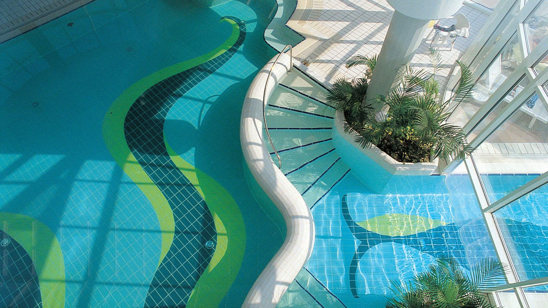 Indoor pool with wavy stairs and plants near large glass windows