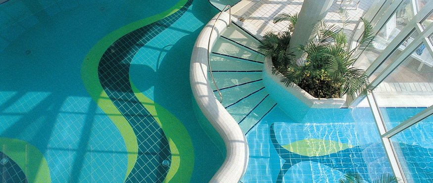 Indoor pool with wavy stairs and plants near large glass windows