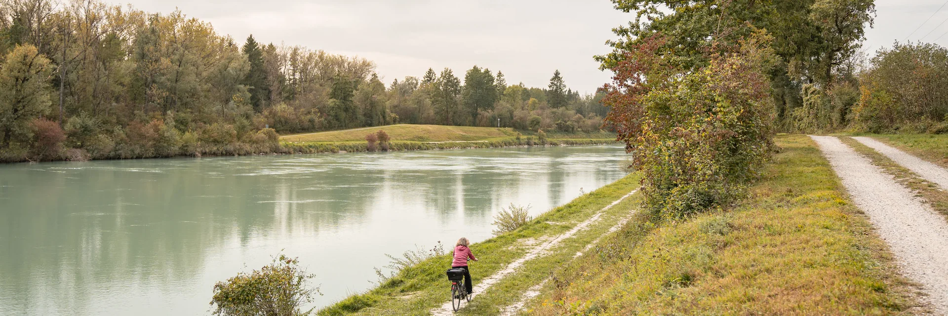 Persoon fietst langs een smal pad bij een rivier met bomen