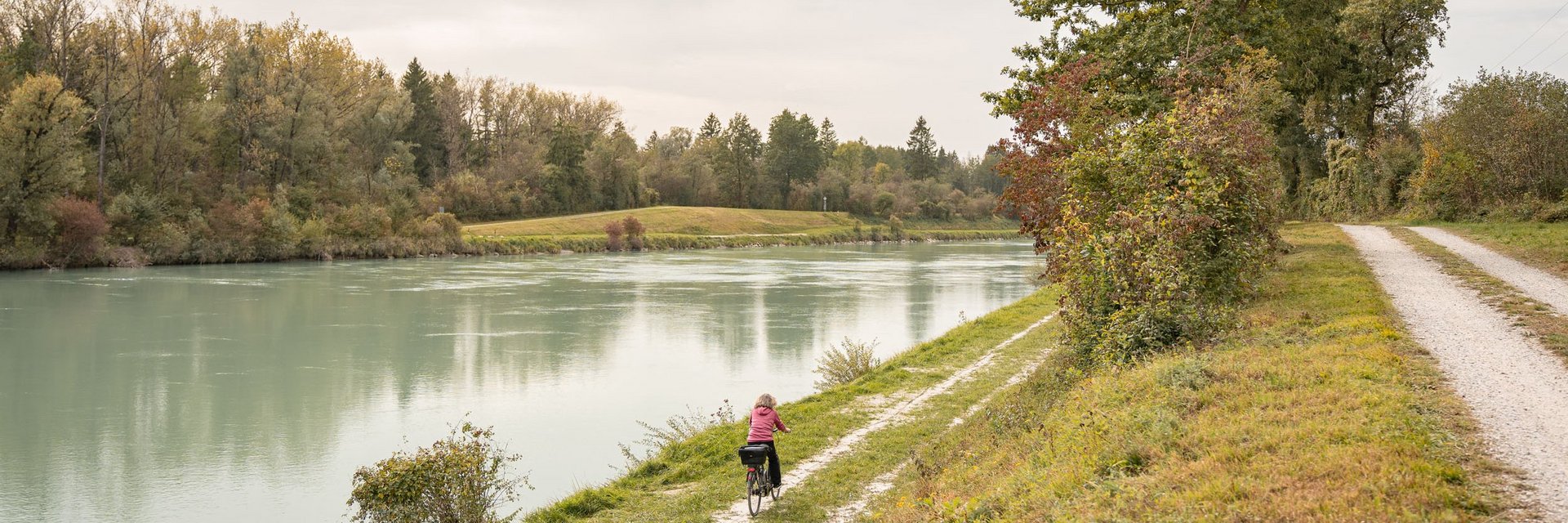 Person cycling along a narrow path by a river with trees