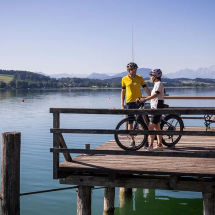 Herbstgenuss im Salzburger Seenland © Heiko Mandl Zwei Radfahrer auf einem Steg am See mit Bergen im Hintergrund