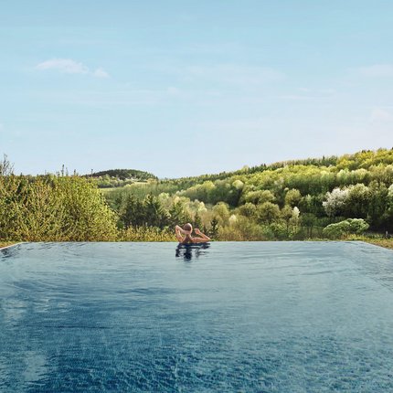 Person relaxing in infinity pool overlooking wooded hills