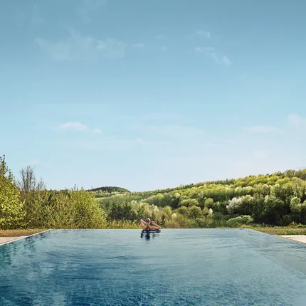 Person entspannt im Infinity-Pool mit Blick auf bewaldete Hügel