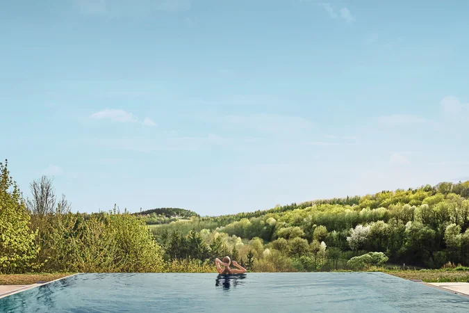 Person entspannt im Infinity-Pool mit Blick auf bewaldete Hügel