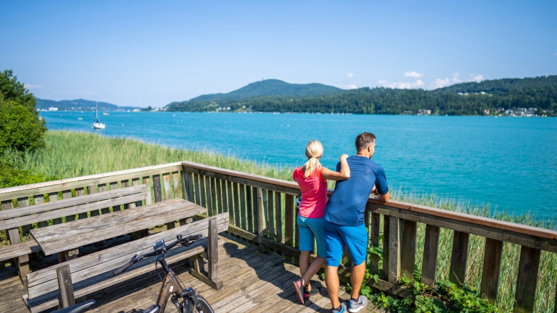 Couple looking at lake from wooden deck with bikes on a sunny day