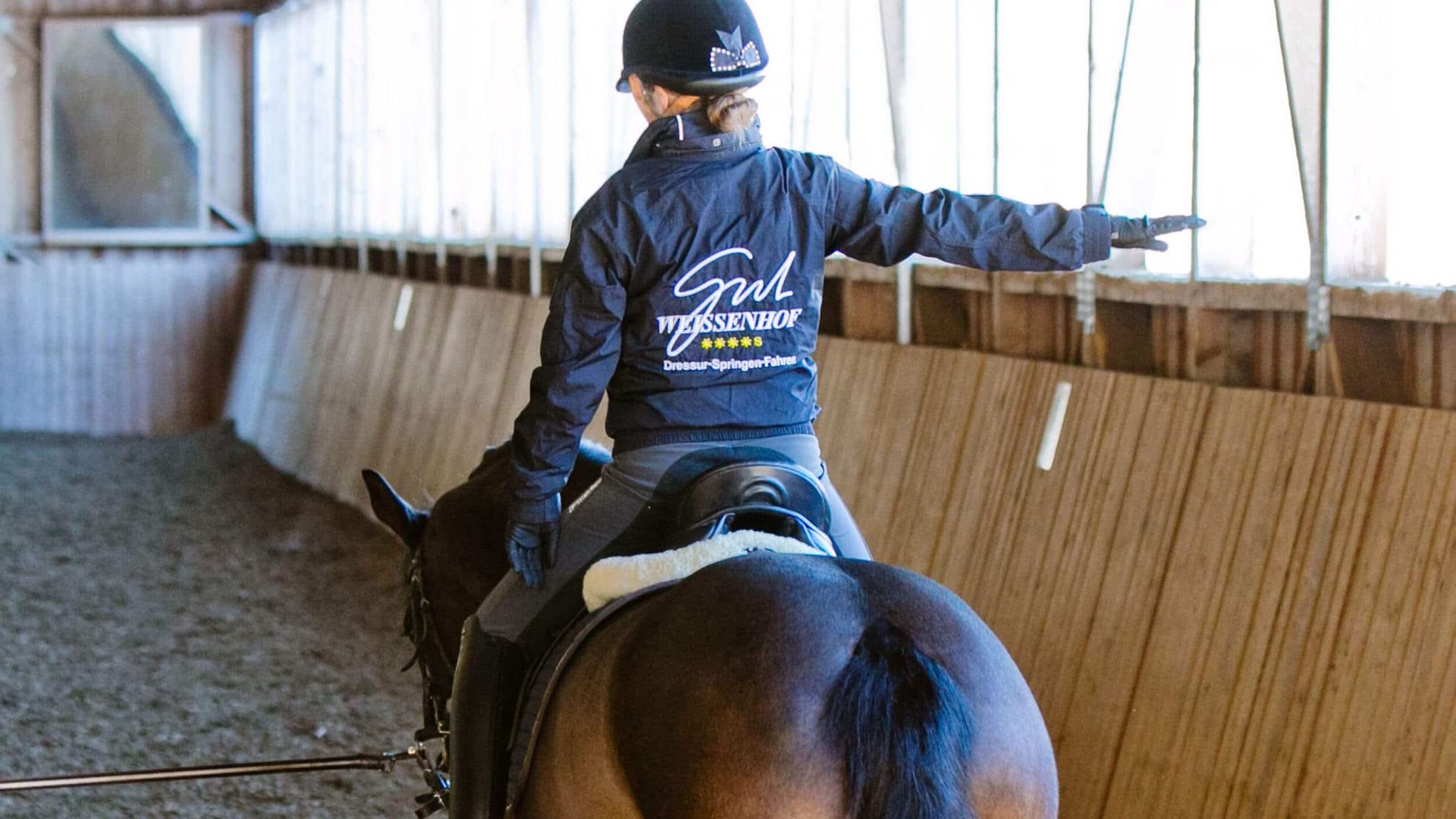 Rider on horse in indoor arena pointing to the right