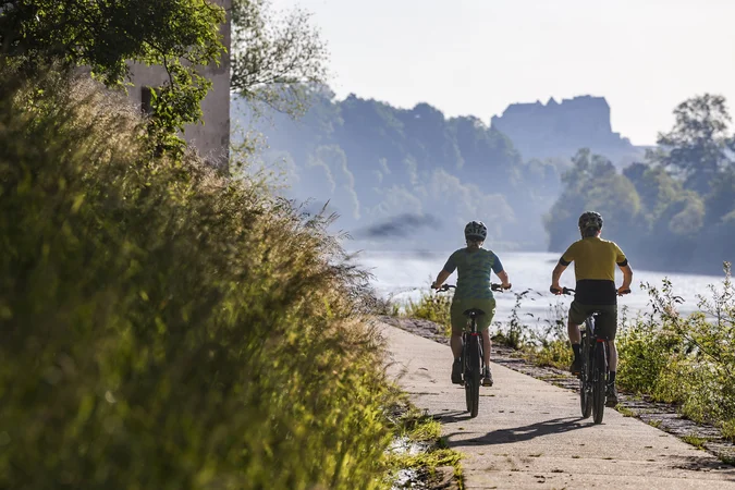 Zwei Radfahrer auf einem Flussweg bei sonnigem Wetter