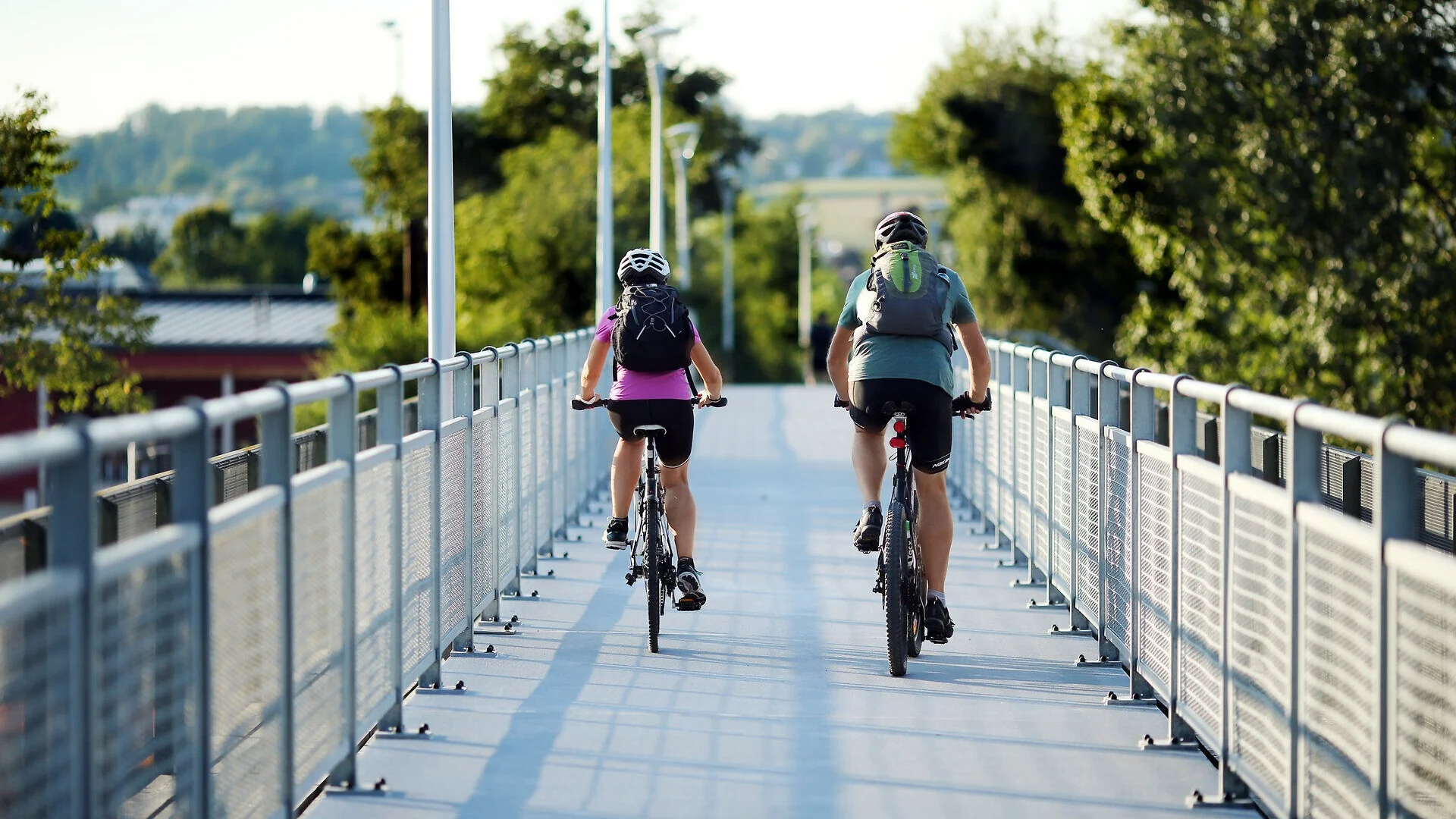 Tour-Detail Zwei Radfahrer mit Helmen und Rucksäcken fahren auf einem Brückenweg bei Tageslicht
