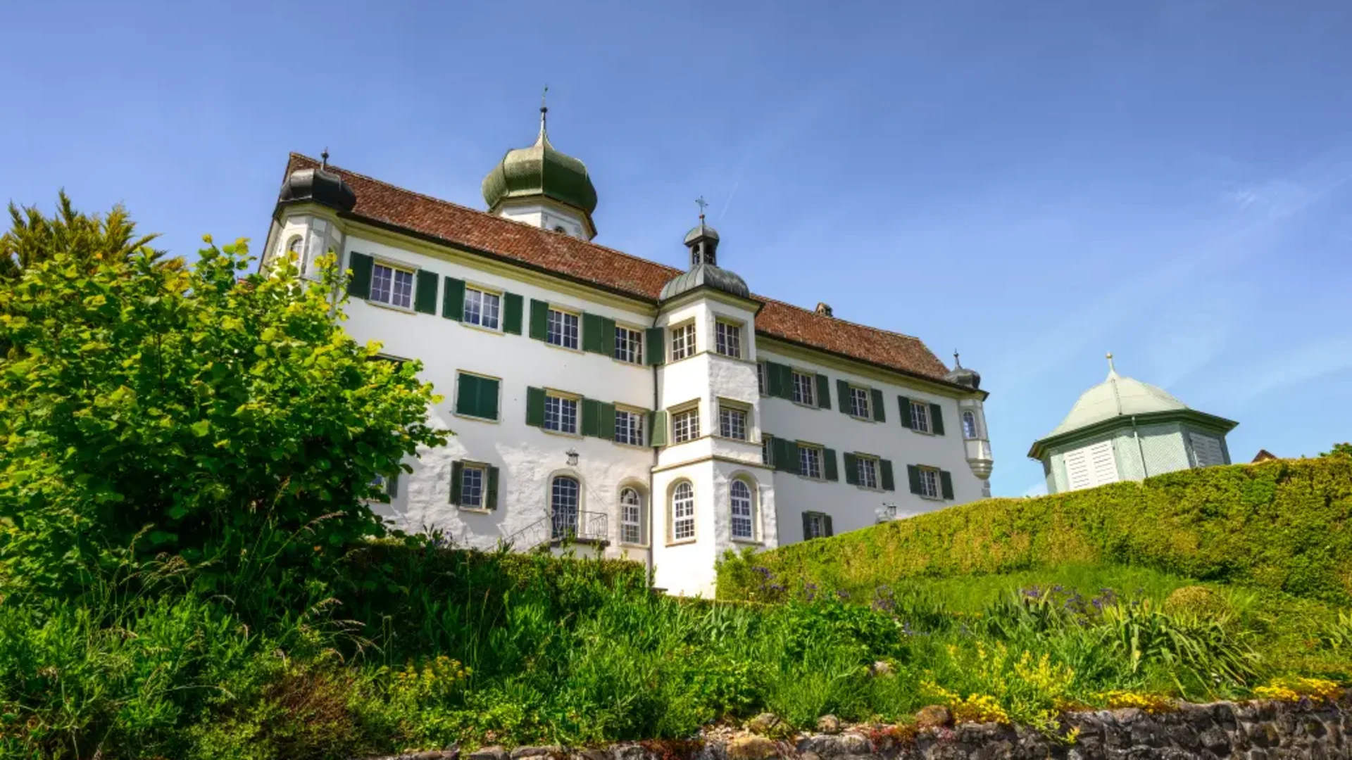 Tour-Detail © Balz Kubli Historisches Gebäude mit grünen Fensterläden und Zwiebelturm bei klarem Himmel