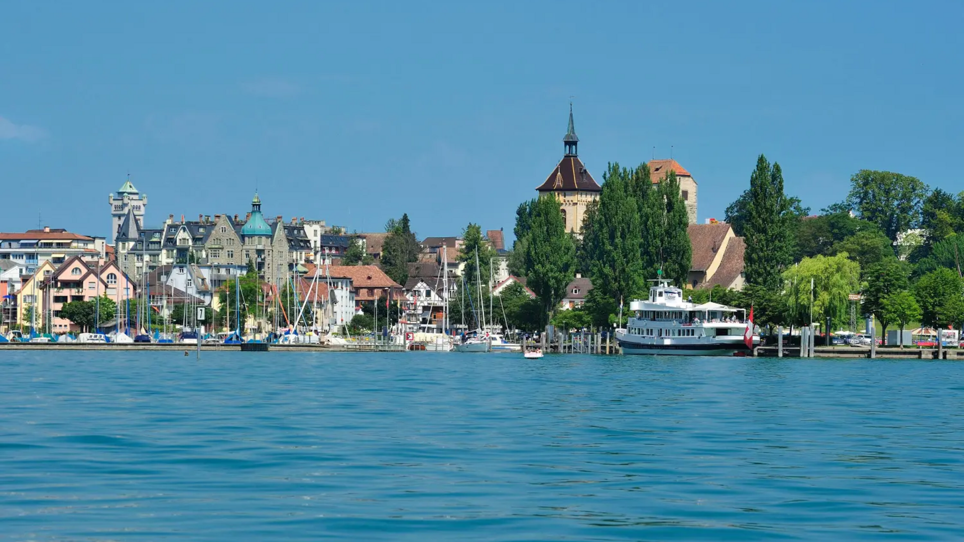 Cityscape by the lake with boats, historic buildings, and clear blue sky