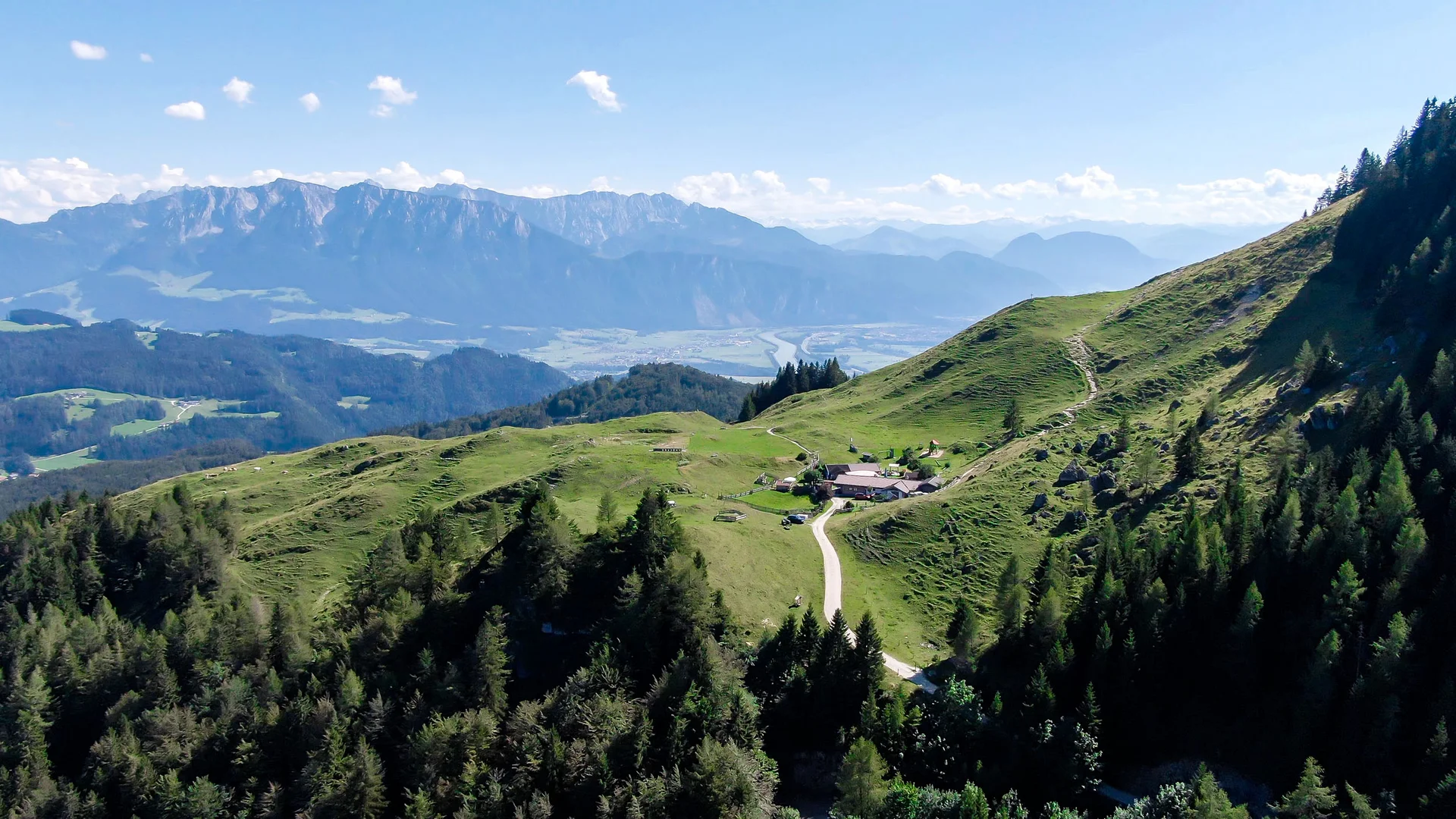 Berglandschaft mit grünem Tal, Hütten und Bergen im Hintergrund