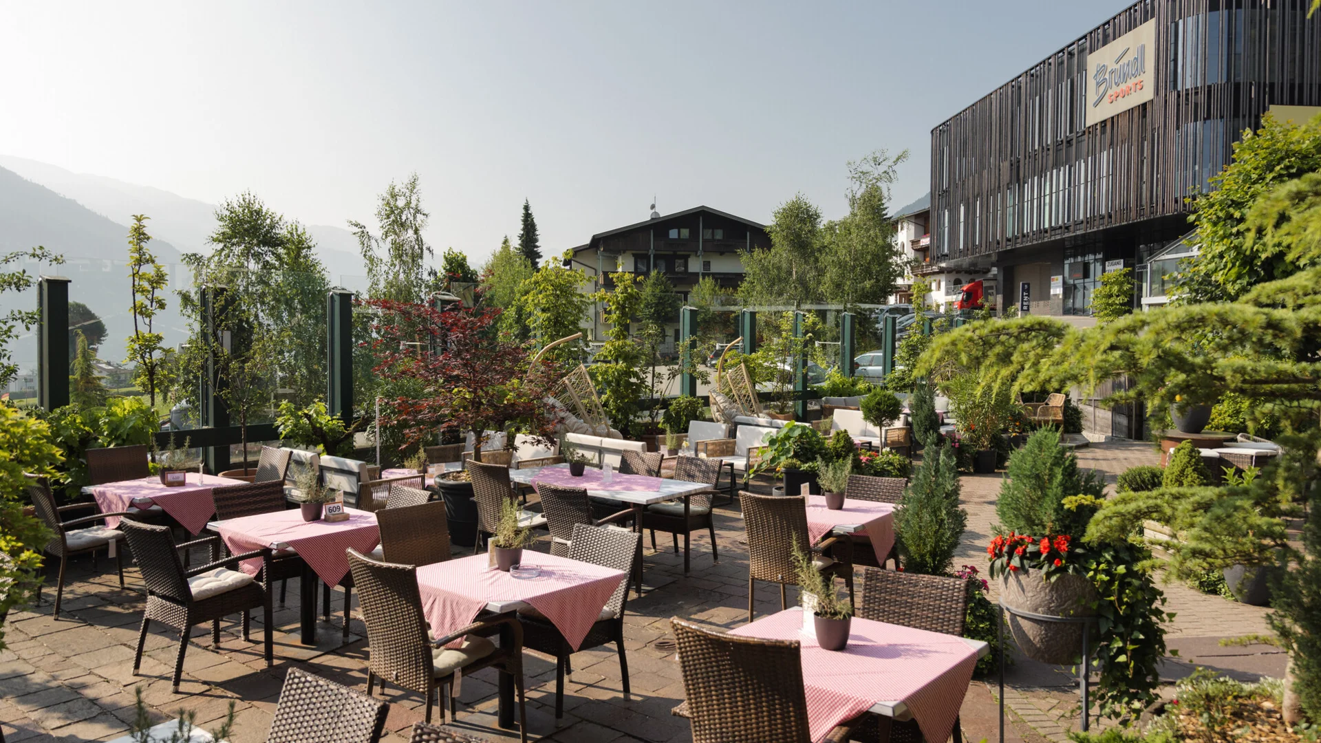 Außenterrasse eines Cafés mit Tischen, Stühlen und Pflanzen an sonnigem Tag