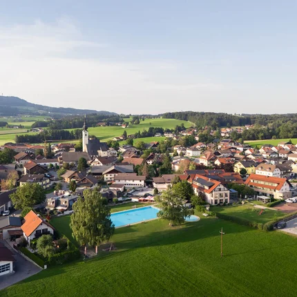 Luchtfoto van een dorp met zwembad en groene velden onder blauwe lucht