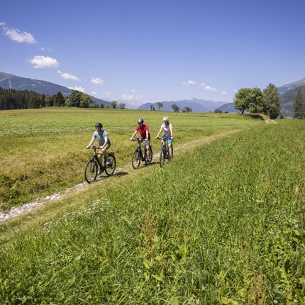 Three cyclists riding on a path through green meadows in the mountains