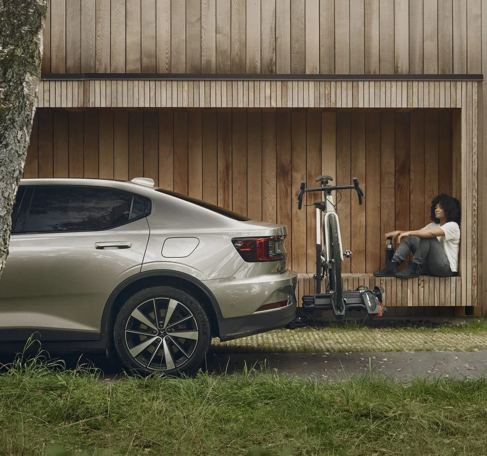 Der Thule Epos © Thule Person sitzt neben einem Fahrrad an einer Holzfassade, daneben steht ein Auto