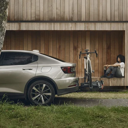 Der Thule Epos © Thule Person sitzt neben einem Fahrrad an einer Holzfassade, daneben steht ein Auto