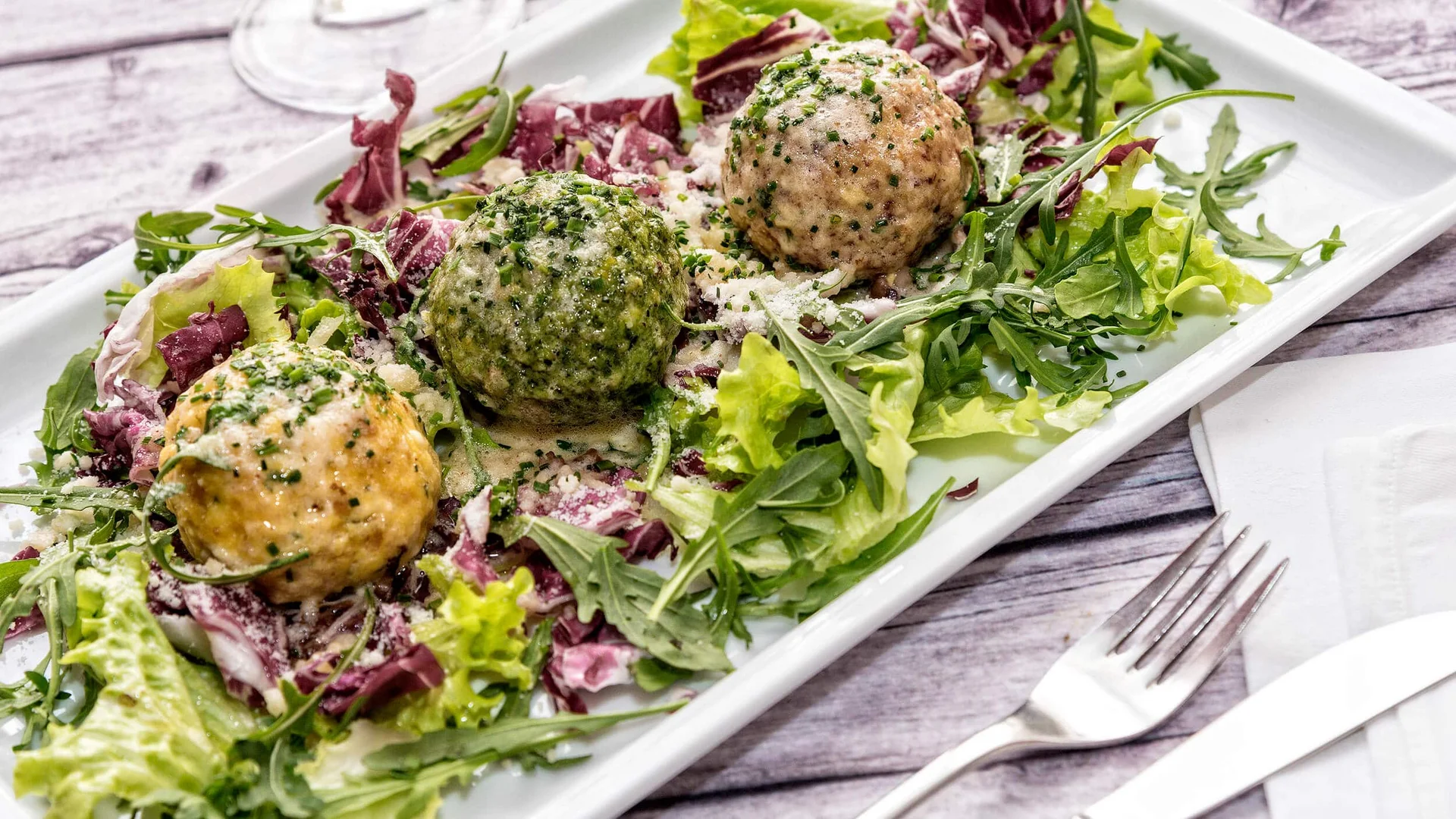 Drie knödel geserveerd op gemengde blaadsla op wit bord