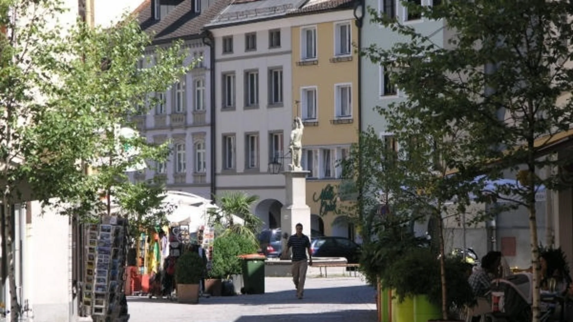 Fußgängerzone mit Bäumen und historischen Gebäuden bei Sonnenschein