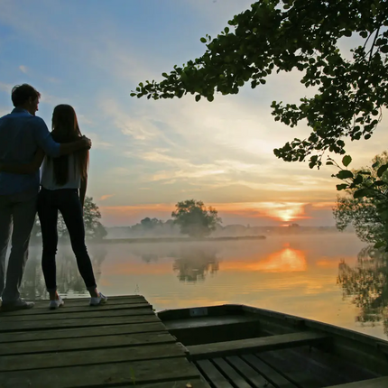 Couple stands on dock watching sunset over calm lake