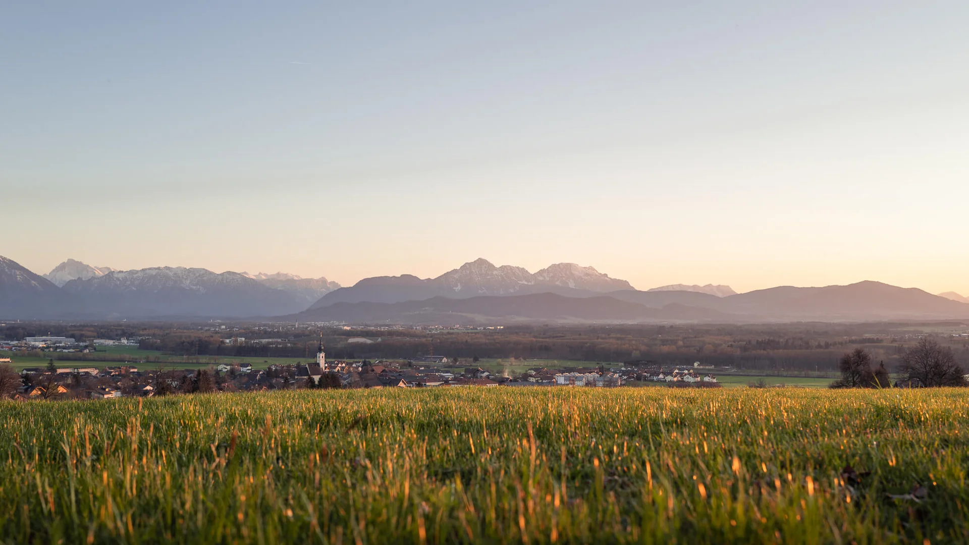 Maunzteufltour © Jakob Eder Grünes Feld mit Dorf und Bergpanorama im Sonnenuntergang
