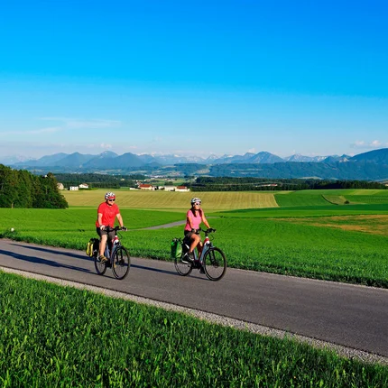 Twee fietsers rijden op landweg door groene velden met bergen op de achtergrond