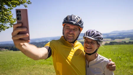 Paar mit Fahrradhelmen macht Selfie auf grünem Feld bei sonnigem Wetter