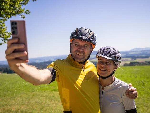 Paar mit Fahrradhelmen macht Selfie auf grünem Feld bei sonnigem Wetter