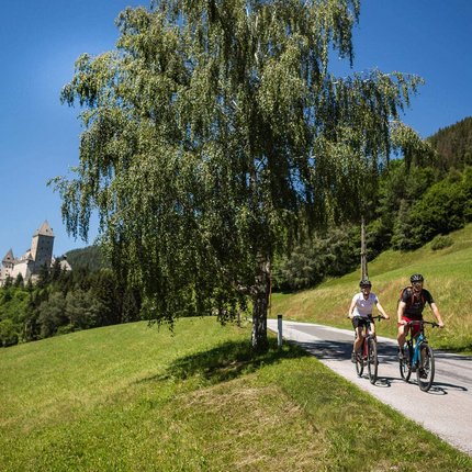 Two cyclists on country road in green landscape with castle in background