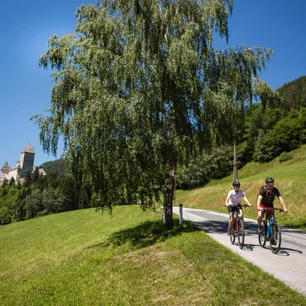 Twee fietsers op landweg in groen landschap met kasteel op de achtergrond