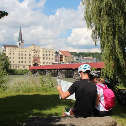 Two cyclists reading a map by river with red bridge and historic buildings