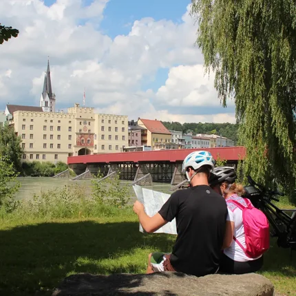 Twee fietsers lezen een kaart bij rivier met rode brug en historische gebouwen