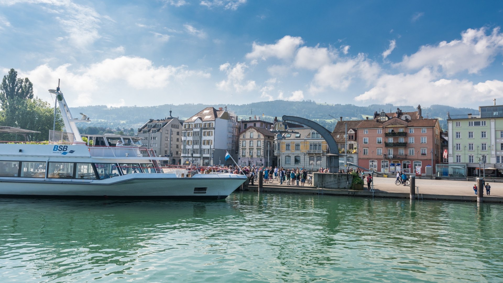 Passenger boat docked at harbor with people and historic buildings nearby