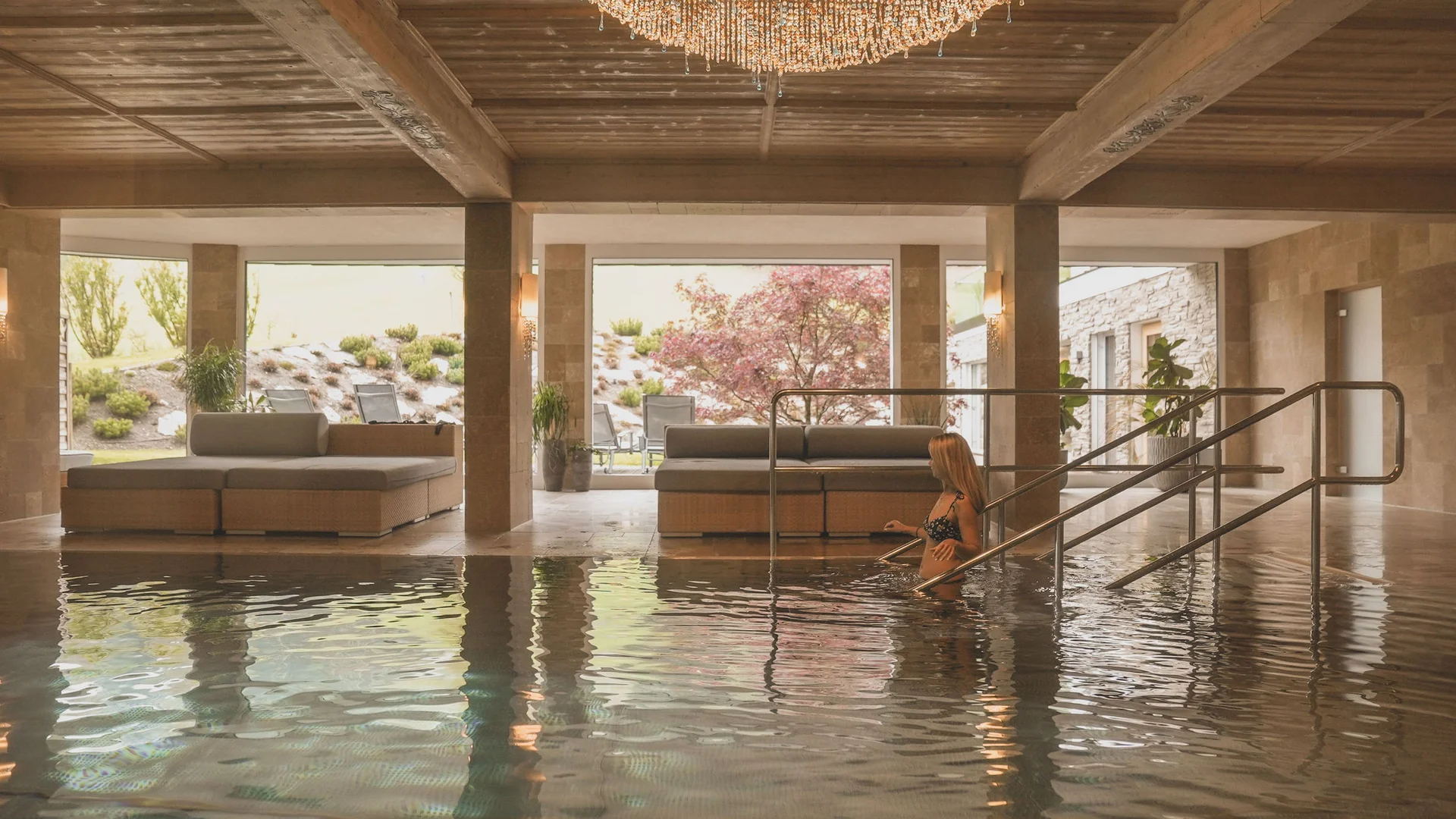 Hotel Thierseerhof **** Woman entering an indoor luxury pool with large windows and chandelier