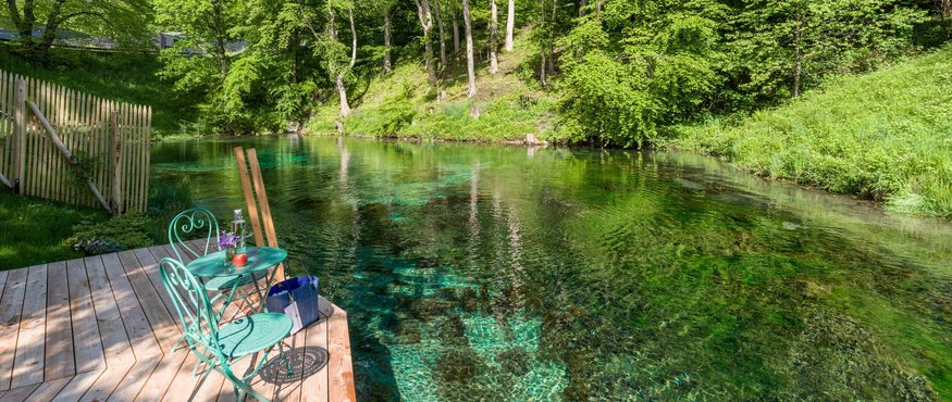 Green chair and table on wooden deck by clear river in forest