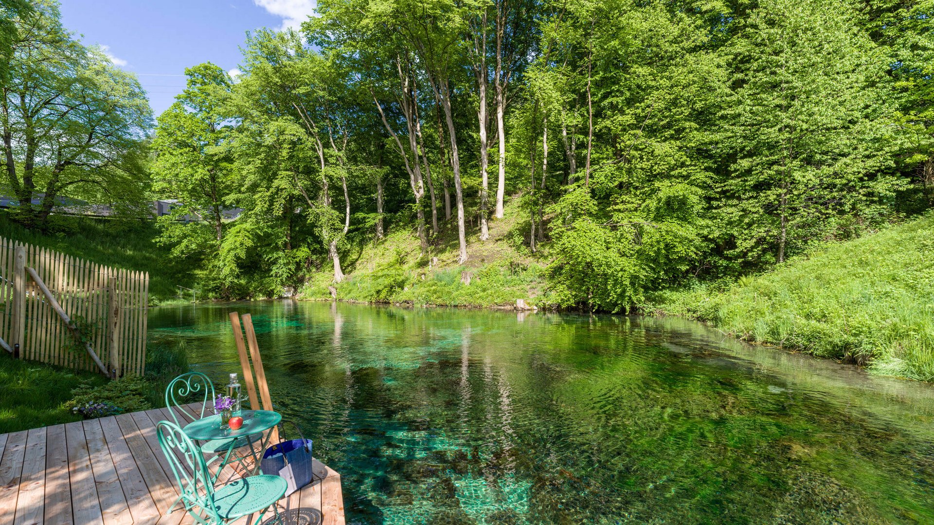 Green chair and table on wooden deck by clear river in forest